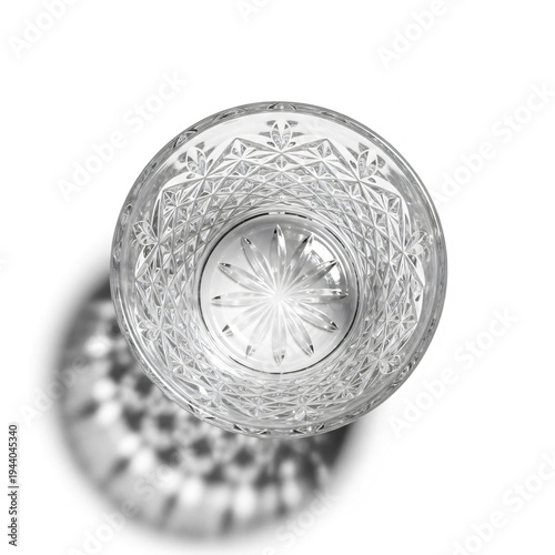 Overhead view of an empty cut crystal glass casting a decorative shadow on a white background, highlighting its intricate patterns.