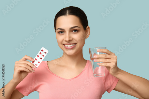 Pretty young woman holding blister pack of vitamin A capsules and glass of wa...