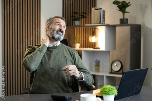Vászonkép Mature man suffering from neck pain and stiffness while working on his laptop in