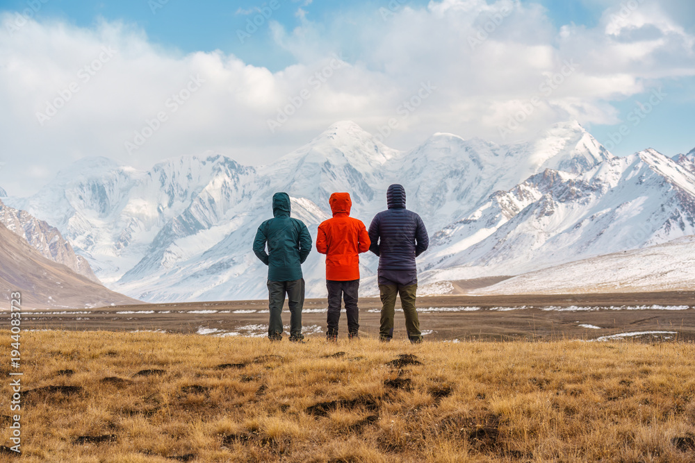 Obraz premium Three mountaineers admiring the majestic snow capped mountain range in Sary Jaz valley during autumn