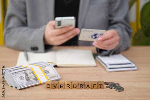 Canvastavla A person in business attire balances their finances at a wooden desk, holding a smartphone in one hand and a bank card in the other, surrounded by cash, coins, and important notes