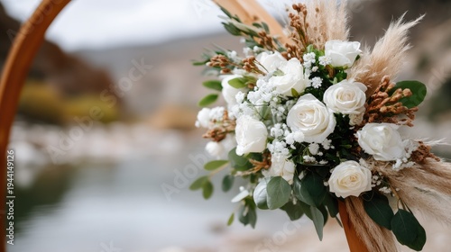 Beautiful wedding ceremony decor with pampas grass and white roses on a wooden arch, set against a river during sunset