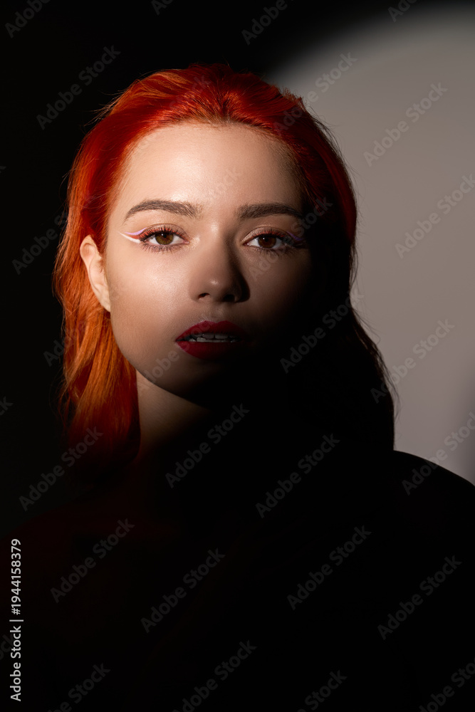 Fototapeta premium Captivating portrait of a stylish young woman with vibrant red hair in soft lighting