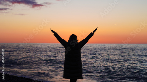 Canvas Print Silhouette of woman with arms raised at sunset by the ocean