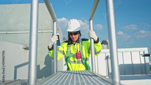 Young woman engineer climbing a metal ladder to inspect industrial equipment, emphasizing safety standards and maintenance operations