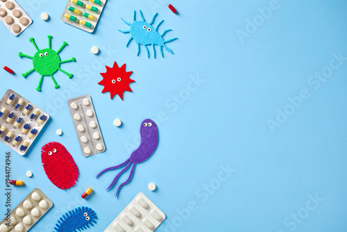 Colorful felt germs with pharmaceutical pills and capsules on blue background. Creative medical concept of virus treatment and antibiotic therapy with copy space.