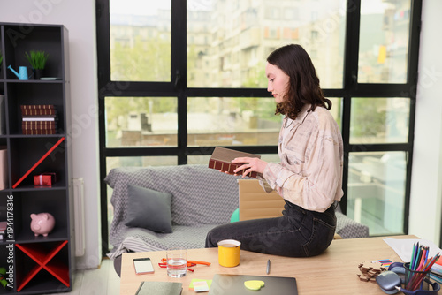 Фотография In a bright, stylish apartment, a woman sits on her desk while exploring a cherished book