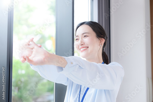 Fotografía 新緑の会社の窓際で伸びやストレッチする休憩するビジネスシーンの女性　スッキリして気分爽快