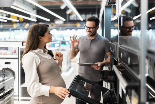 Obraz na plátně A pregnant woman chooses a new built-in oven in a home appliance store while a male assistant provides professional advice and makes an ok gesture
