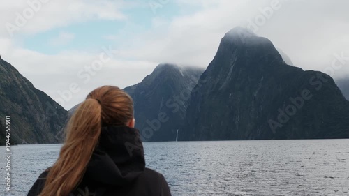 Female traveler enjoying scenic boat cruise in Milford Sound fjord with Mitre Peak mountains, New Zealand
