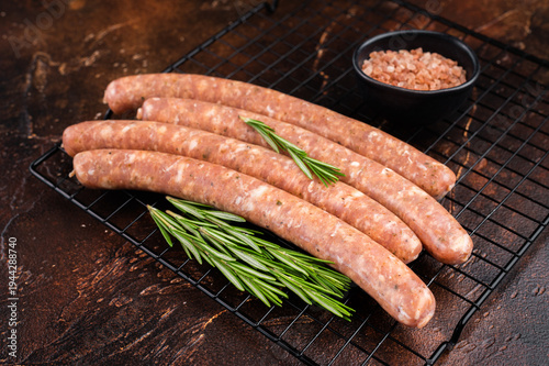 Valokuva Raw fresh Chipolata sausages on metal grill rack with rosemary and coarse salt on dark rustic background