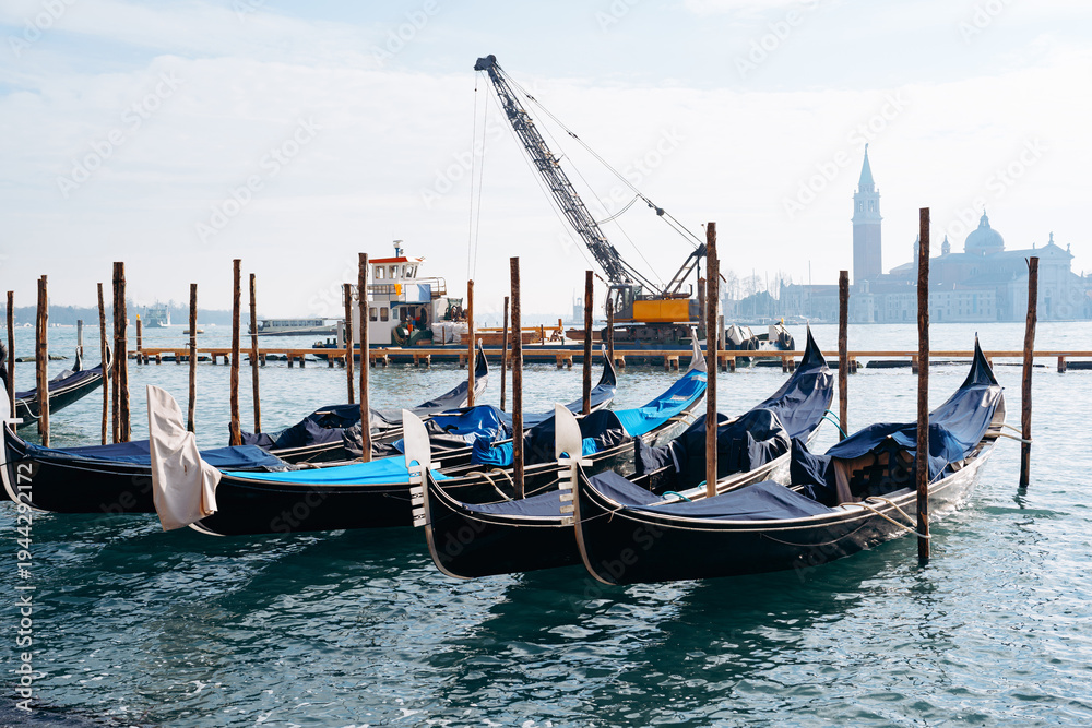 Fototapeta premium Gondolas moored at waterfront with cranes and buildings in the background during daytime in Venice