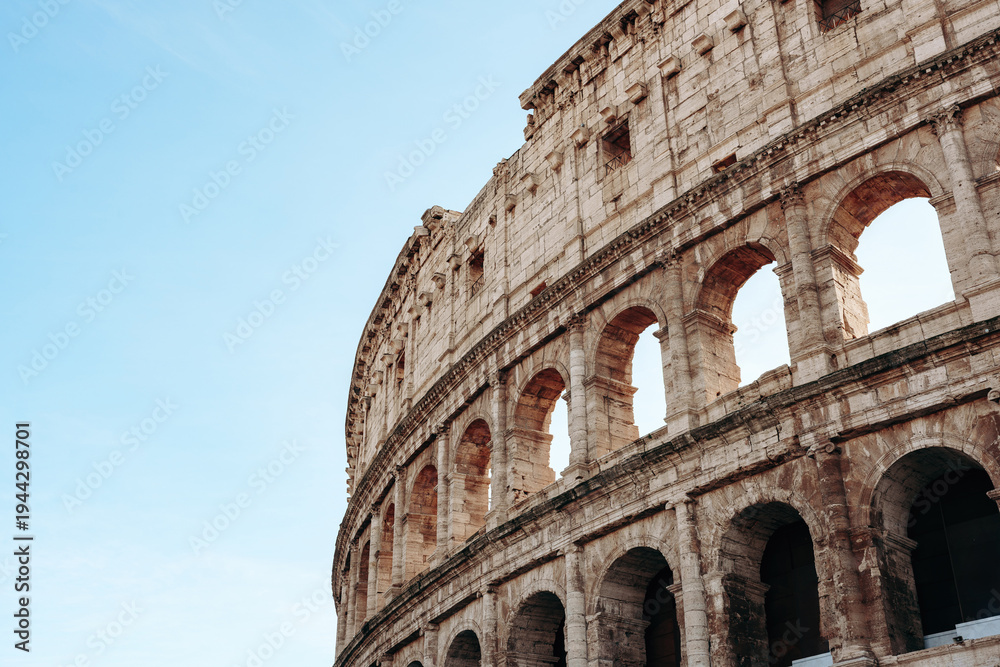 Fototapeta premium Historic Roman Colosseum stands tall under blue sky in Rome, Italy during the day