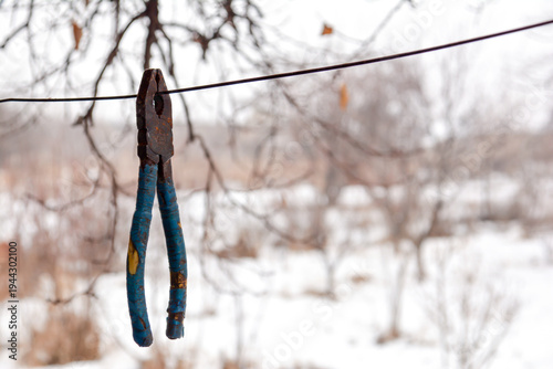 A pair of pliers hanging on a wire against the background of a winter landscape