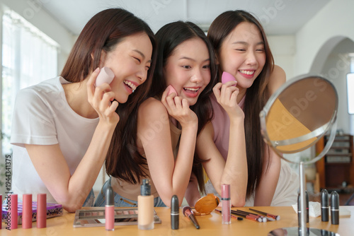 Asian women friends applying makeup with sponge together in front of mirror
