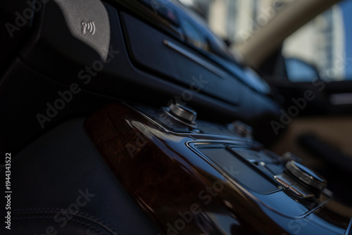 Car central console with glossy wood trim and rotary control knobs on modern automobile interior panel.