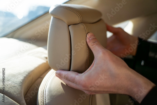 Passenger adjusting side support of rear seat headrest in luxury car interior.