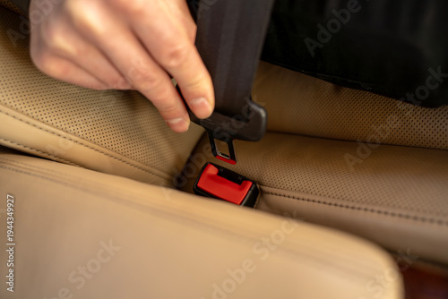 Passenger inserting seat belt into buckle while sitting in rear seat of luxury sedan.