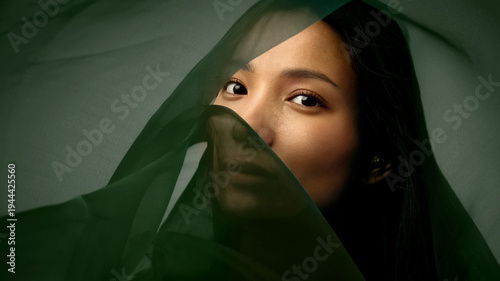 Quadro su tela Cinematic beauty portrait of Asian woman emerging from dark green silk fabric symbolizing transformation and renewal for luxury skincare advertising, wellness branding and beauty campaigns