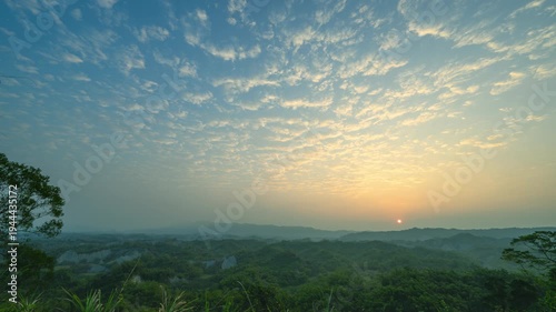 A breathtaking sunrise over the misty hills and lush forests of Erliao Lookout in Tainan, Taiwan, featuring a soft golden sky.