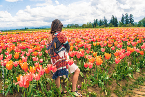 A woman stands in a field of flowers, wearing a colorful jacket and shorts