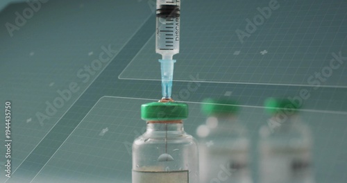 Withdrawing medication from glass vial with green cap at lab bench, showing droplet on syringe tip