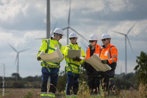 Engineer and technicians analyzing wind turbine project using blueprint at renewable energy farm during sunset. Teamwork in sustainable power industry, clean energy technology development.