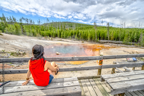 A woman sits on a wooden bench overlooking a hot spring