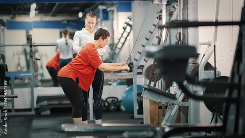 Personal trainer assisting senior woman with cable machine workout