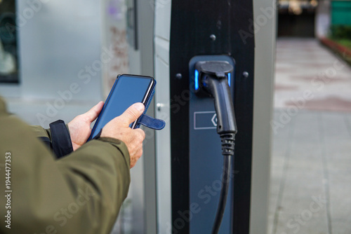 Charging electric car at EV station using smartphone app, modern electric mobility