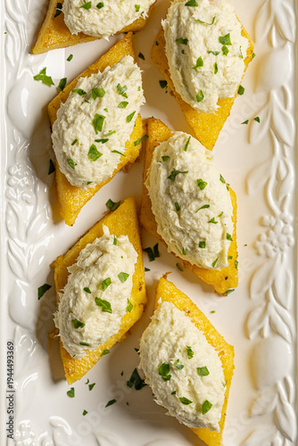 Top view of baccala mantecato, whipped, creamed salt cod fish spread, is a Venetian appetizer made with dried cod, served on fried polenta croutons. Verttical image.