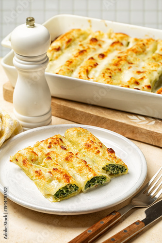 Lunch with baked Cannelloni, cylindrical type of egg-based pasta stuffed  with spinach and ricotta, covered by cheese and bechamel  sauce in Italian cuisine. Vertical image.