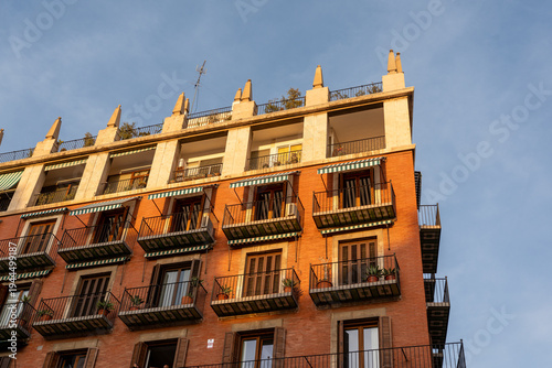 Low angle view of a traditional brick apartment building with balconies and awnings in warm sunset light in Valencia, Spain, suitable for urban architecture and travel designs.