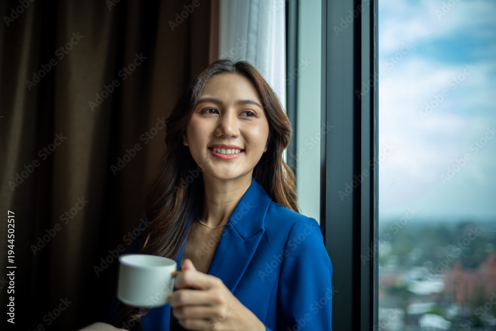 Naklejka premium Young businesswoman standing by a window, holding a cup and smiling