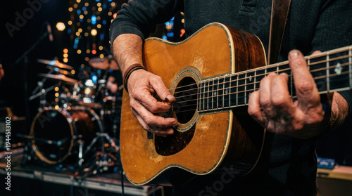 Passionate musician playing wooden acoustic guitar with focused hand movement on live concert stage delivering an energetic music performance in dark venue