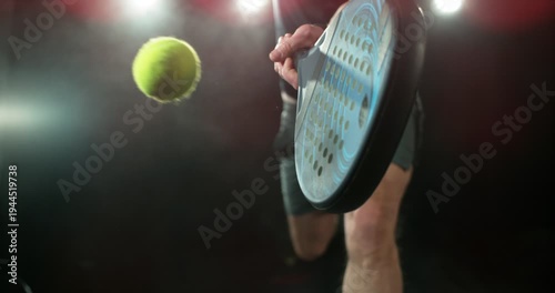 Super slow motion close-up of a padel player hitting a ball with a racket, filmed at 1000 fps. Dramatic studio lighting highlights the impact, motion and energy of the sport in a dynamic action