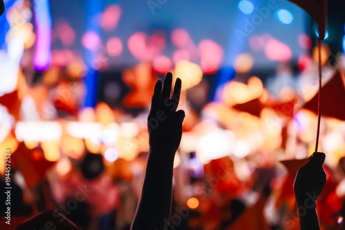 Supporter holding a pen and raising a three-finger salute at the People's Party (Phak Prachachon) rally in Thailand. Crowd with orange flags and phone lights for February 8, 2026 election.