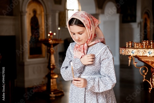 Картината върху платно a child girl prays crossing herself in an Orthodox church holding a candle, a be