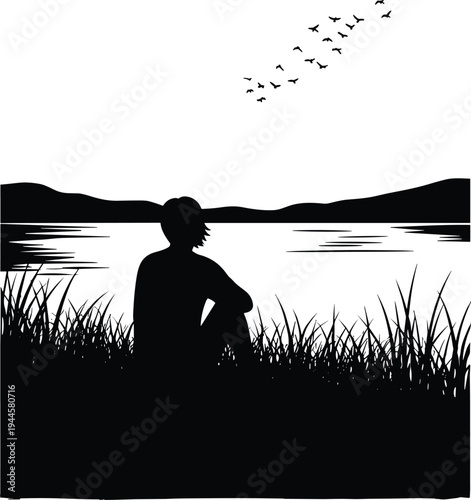 Black silhouette of a person sitting in grass by a lake watching birds flying over mountains for mindfulness peace and solitude nature concept