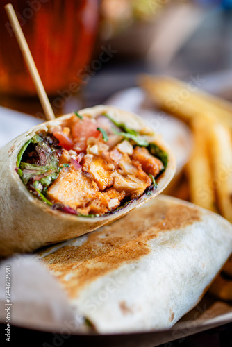 A buffalo chicken wrap with tomatoes lettuce red onion served with fries at a modern restaurant and cafe 