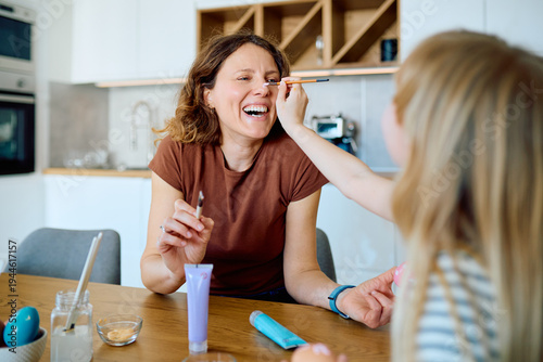 Fotografi Daughter lovingly painting mother's face with a brush, creating happy family mom