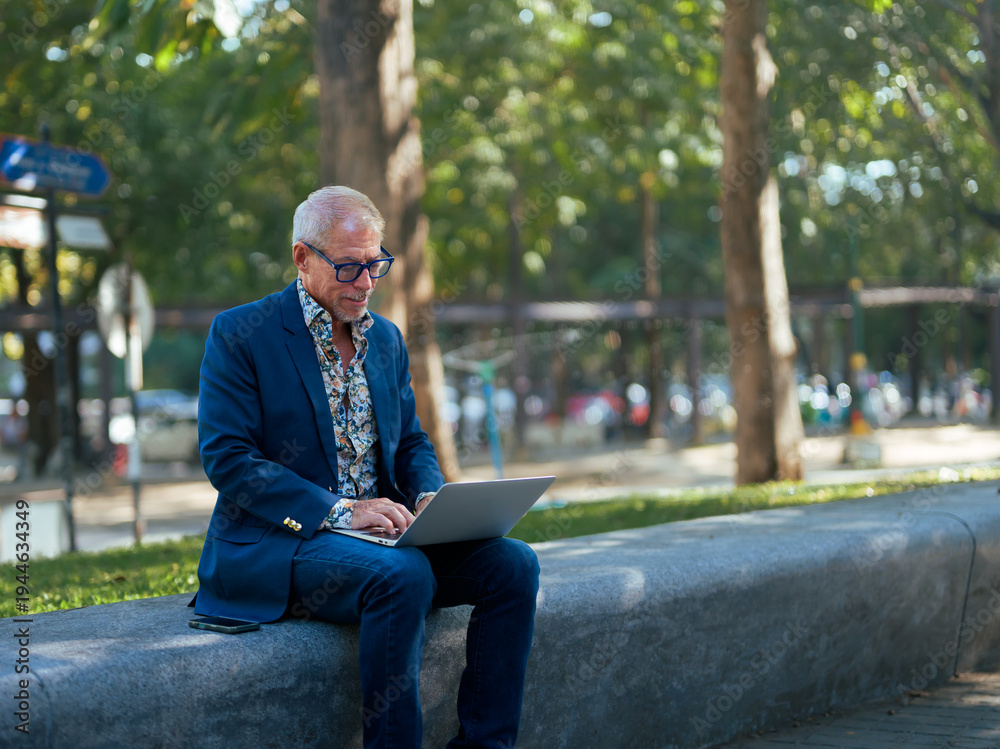 Fototapeta premium Senior man working remotely on laptop outdoors in park