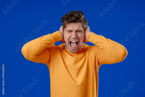 Mature man Covering Ears, Showing Irritation In Blue Studio. Stress, Overload
