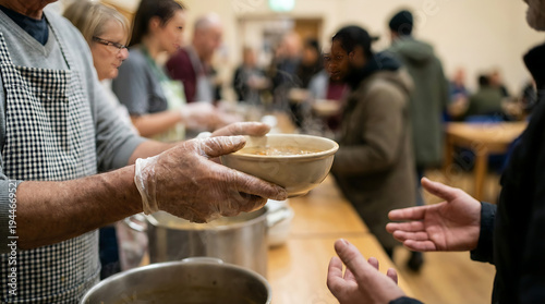 Hands of a volunteer with a compassionate and helpful mood handing a warm bowl of soup to a person in need representing community support and kindness on a blurred soup kitchen background.