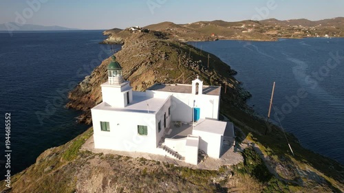 Drone aerial view circling the lighthouse and small chapel above Korissia harbor on Kea Island in the Cyclades, Greece, overlooking the Aegean Sea.