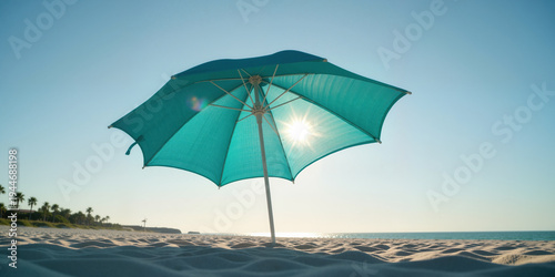 Teal beach umbrella on white sandy shore facing calm ocean waters under bright sunny clear blue sky.