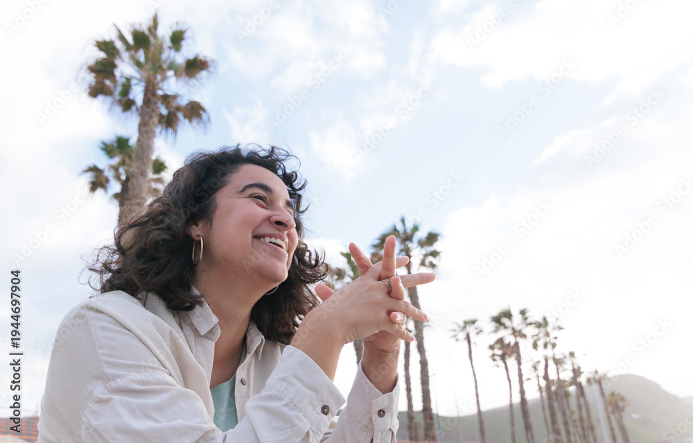 Fototapeta premium A dark-haired girl with curly hair smiles happily at sunset in an outdoor area with palm trees.