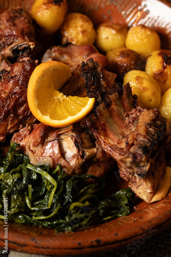 Roast kid goat, a traditional dish from northern Portugal, served with golden potatoes, sautéed greens, and a fresh orange slice, highlighting rustic flavors and hearty regional cuisine.