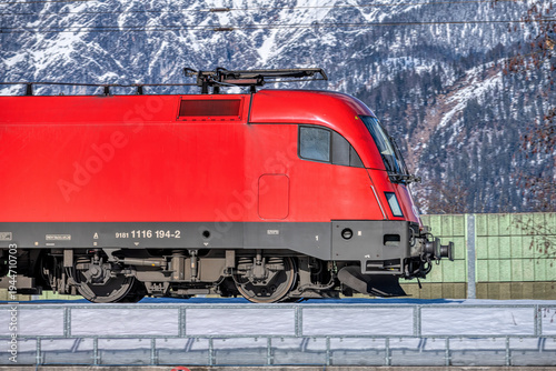 red electric locomotive taurus in front of snow covered alpine mountains, modern railway transport and logistics in austria, close up of train engine with mountain landscape background