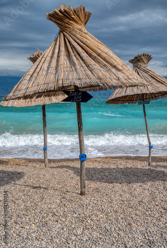 Εκτύπωση καμβά straw beach umbrellas on a pebbly shore at the adriatic sea, tropical coastal la